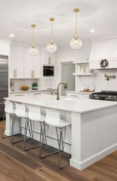 a large kitchen with white cabinets and counter tops, along with bar stools that match the hardwood flooring