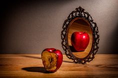 an apple sitting in front of a mirror on top of a wooden table next to a piece of fruit