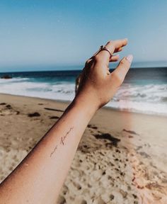 a person's hand on the beach with waves in the background