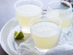 two glasses of lemonade sit on a white plate with limes next to it