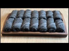 a wooden board topped with lots of rolled up black towels on top of a table