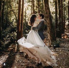 a bride and groom standing in the woods with their wedding dress blowing in the wind