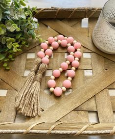 pink and white beads with tassels on a wooden tray next to a potted plant