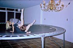 two women are doing tricks on a trampoline in a room with chandelier