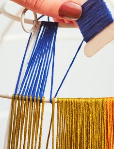 a hand is holding two different colored threads on a white piece of wood and metal