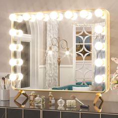 a vanity mirror with lights on it in front of a counter top and vase filled with flowers