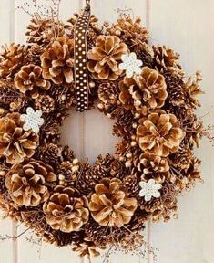 a pine cone wreath hanging on a white door with snowflakes and other decorations