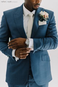 a man in a blue suit and white flower boutonniere is looking at his watch