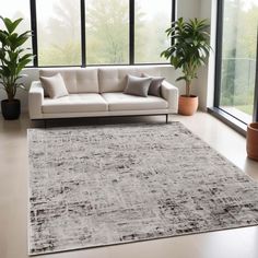 a living room with a couch, rug and potted plants on the floor in front of large windows