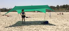 a woman standing under a green tent on the beach