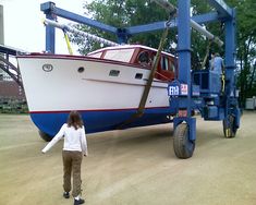 a woman standing in front of a boat being lifted by a crane on a truck