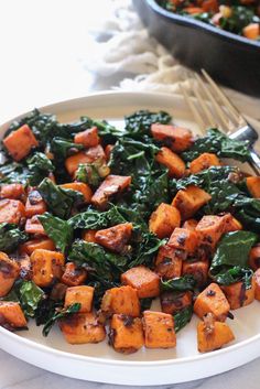 a white plate topped with tofu and spinach next to a skillet filled with other food