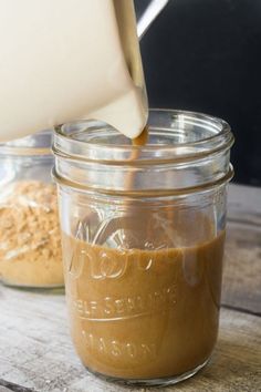 a glass jar filled with peanut butter and topped with an oatmeal being poured into it