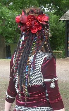 a woman with long dreadlocks and flowers on her head is walking in the park