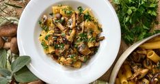 pasta with mushrooms and parsley in a white bowl next to other vegetables on a table