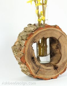 a vase filled with yellow flowers sitting on top of a piece of tree trunk in front of a white background