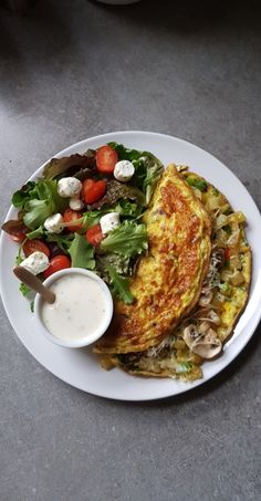 an omelet and salad on a white plate with a side of ranch dressing