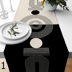 a black and white table runner with an abstract design on it, next to a plant