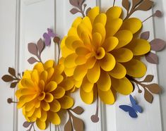 two paper flowers on a white door with blue butterflies around the petals and one yellow flower