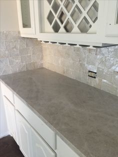 a kitchen counter top with white cabinets and marble tile backsplash in the background