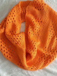 an orange crocheted scarf laying on top of a white bed sheet with a knot in the middle