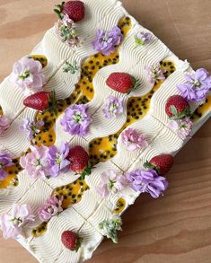 a cake decorated with flowers and strawberries on a wooden table top, ready to be eaten