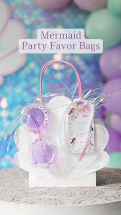 a mermaid party favors bag sitting on top of a white cake with balloons in the background