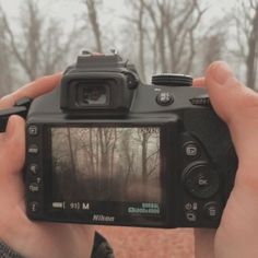 a person holding up a camera to take a photo in front of some trees and bushes