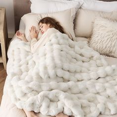 a woman laying in bed under a fluffy white blanket