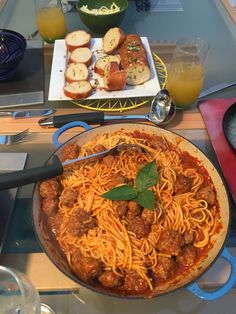 a plate of spaghetti with meatballs, bread and orange juice on a table top