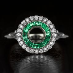 an emerald and diamond ring on a black surface with the center surrounded by white diamonds