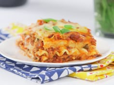 a white plate topped with lasagna next to a glass of water and napkins