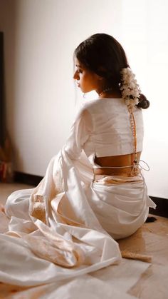 a woman sitting on the floor with her back turned to the camera and wearing a white dress