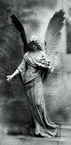 an angel statue with outstretched wings holding a bouquet of flowers in front of a wall