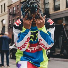 a man with dreadlocks covers his face while standing on the sidewalk in front of a building