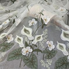 white flowers and green leaves are on the sheered fabric that has been embroidered onto