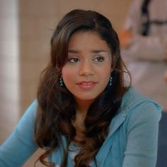 a woman with long dark hair and blue sweater looking at the camera while sitting down