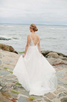 a woman in a wedding dress standing on rocks near the ocean looking at the water