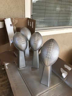 three silver footballs sitting on top of a table in front of a box and window