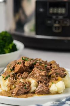 a white plate topped with meat and mashed potatoes covered in gravy next to an instant pressure cooker