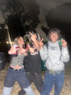 three people standing in the grass with their hands up and one person holding two sodas