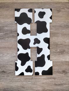 the letter h is made up of black and white cow print paper on a wooden surface