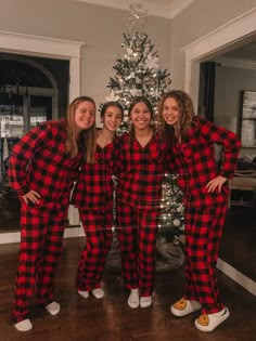 four women in matching pajamas standing next to a christmas tree