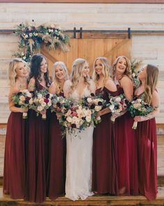 a group of women standing next to each other in front of a wooden door holding bouquets