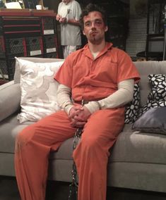 a man in an orange prison outfit sitting on a couch