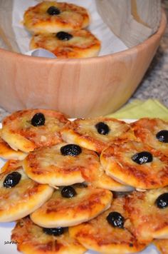 small pizzas with olives and cheese are on a plate next to a bowl