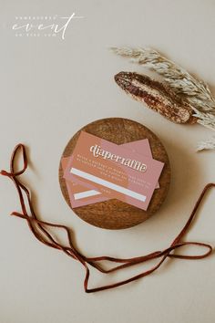 a round wooden box with some pink and white business cards on top of it next to a dried plant