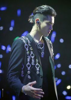 a male in a black jacket and silver earring is standing on stage with his hands out to the side