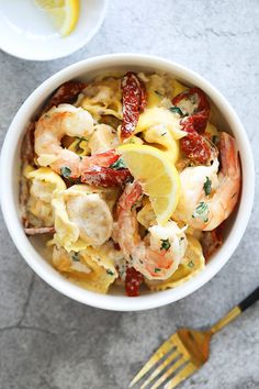 a bowl filled with pasta and shrimp on top of a table next to a fork