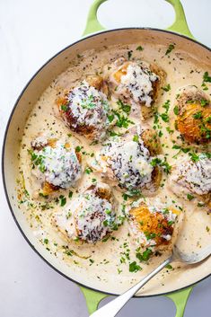 a green pan filled with meatballs covered in gravy and garnished with parsley